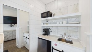 A modern kitchen with white cabinetry, a built-in microwave, a coffee maker, and a stainless steel sink.