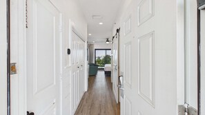 A hallway with white doors, a bed, a chair, and a view of the outside.