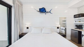 Una habitación de hotel con una cama grande, una kitchenette y una escultura decorativa de un pez en la pared.
