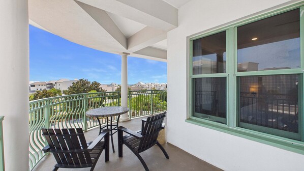 Un balcón con mesa y sillas, vistas a edificios y una ventana con marco verde.