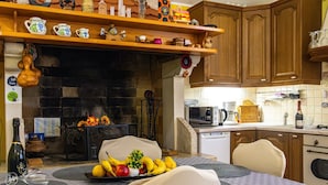 A cozy kitchen with wooden cabinets, a stone fireplace, and a dining table set with placemats and fruit. - House Of Good Vibrations Indy (Galizana)
