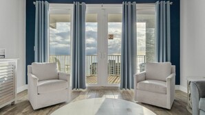 A modern living room with a large sliding glass door leading to a balcony. There are two white armchairs and a small round table in the room.