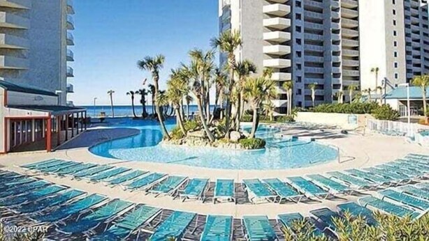 A hotel pool area with sun loungers and palm trees.