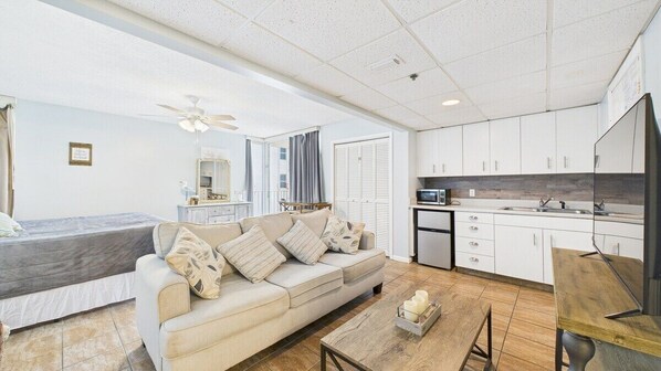 A modern, well-lit room with a sofa, a bed, a small table, and a kitchenette.