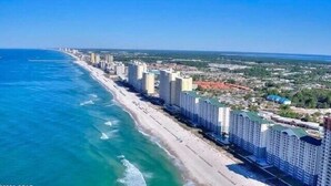 A coastal cityscape with high-rise buildings along the beachfront, a clear blue sky, and a view of the ocean.