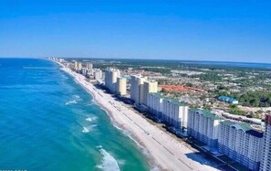 A coastal cityscape with high-rise buildings along the beachfront, a clear blue sky, and a view of the ocean.