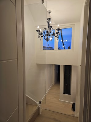 A hallway with a chandelier, a window with a view, and a wooden floor.