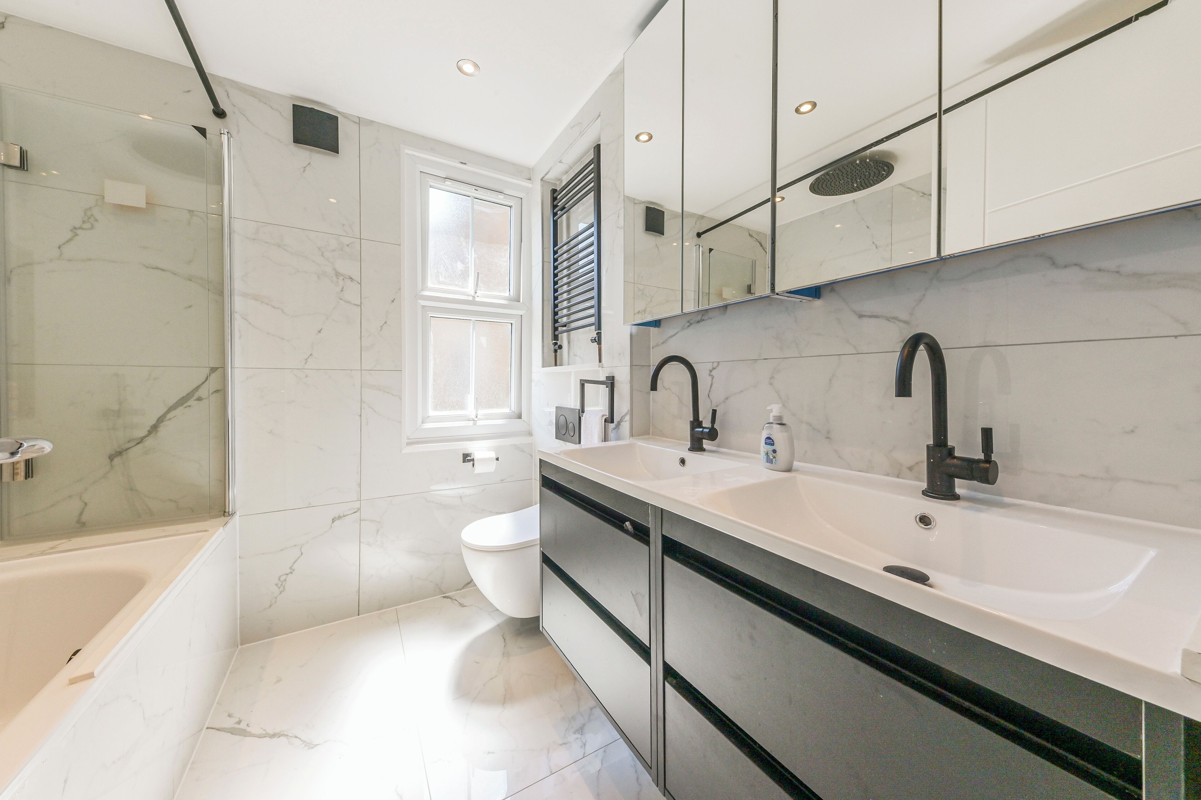 A modern bathroom with a bathtub, two sinks, a toilet, and a shower.