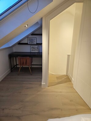 A room with a sloped ceiling, a desk with a chair, and framed artwork on the wall.