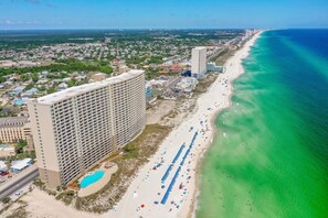 Un paisaje urbano costero con una extensa playa, un hotel grande de varios pisos y un océano azul cristalino.