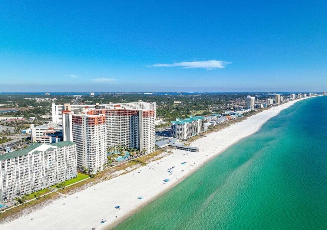 Een kusthotel met meerdere hoge gebouwen, een strand en een helderblauwe lucht.