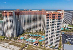 A high-rise hotel with multiple balconies, a central swimming pool, and a view of the ocean. - Reel Paradise 1810–Oceanview–Sleeps 6 (Panama City Beach)
