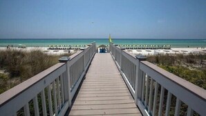 A wooden boardwalk leading to a beach with umbrellas and lounge chairs.