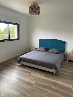 A bedroom with a bed, wooden flooring, a window, and a ceiling light fixture.