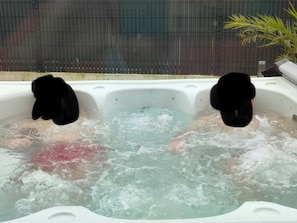 A hot tub with two people, surrounded by a metal fence and a plant.