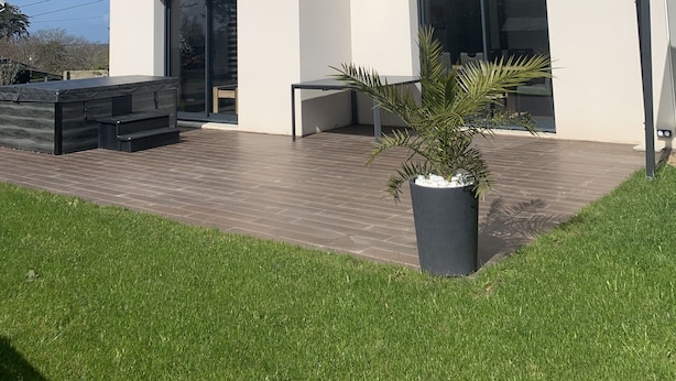 Et moderne hus i to etager med fladt tag, store vinduer og en terrasse med jacuzzi og en potteplante.