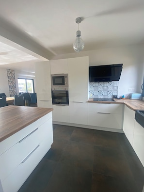 A modern kitchen with white cabinetry, a microwave, oven, and a black range hood.