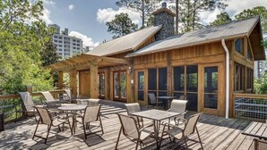 A wooden deck with outdoor seating and a stone chimney. - Bay Watchin 3511- Beach Tram-Sleeps 6 (Miramar Beach)