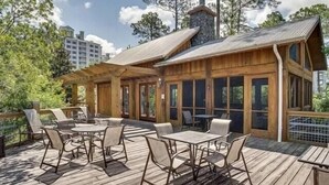 A wooden deck with outdoor furniture, a stone chimney, and a view of surrounding trees. - Bay-Cation 4207-Cozy Studio-Sleeps 4 (Miramar Beach)