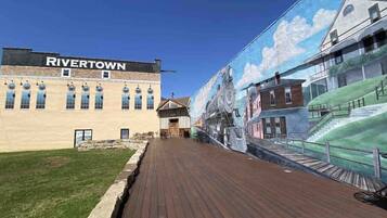 A boardwalk with a mural of a train and buildings, a sign reading "RIVERTOWN", and a building with a flat facade.