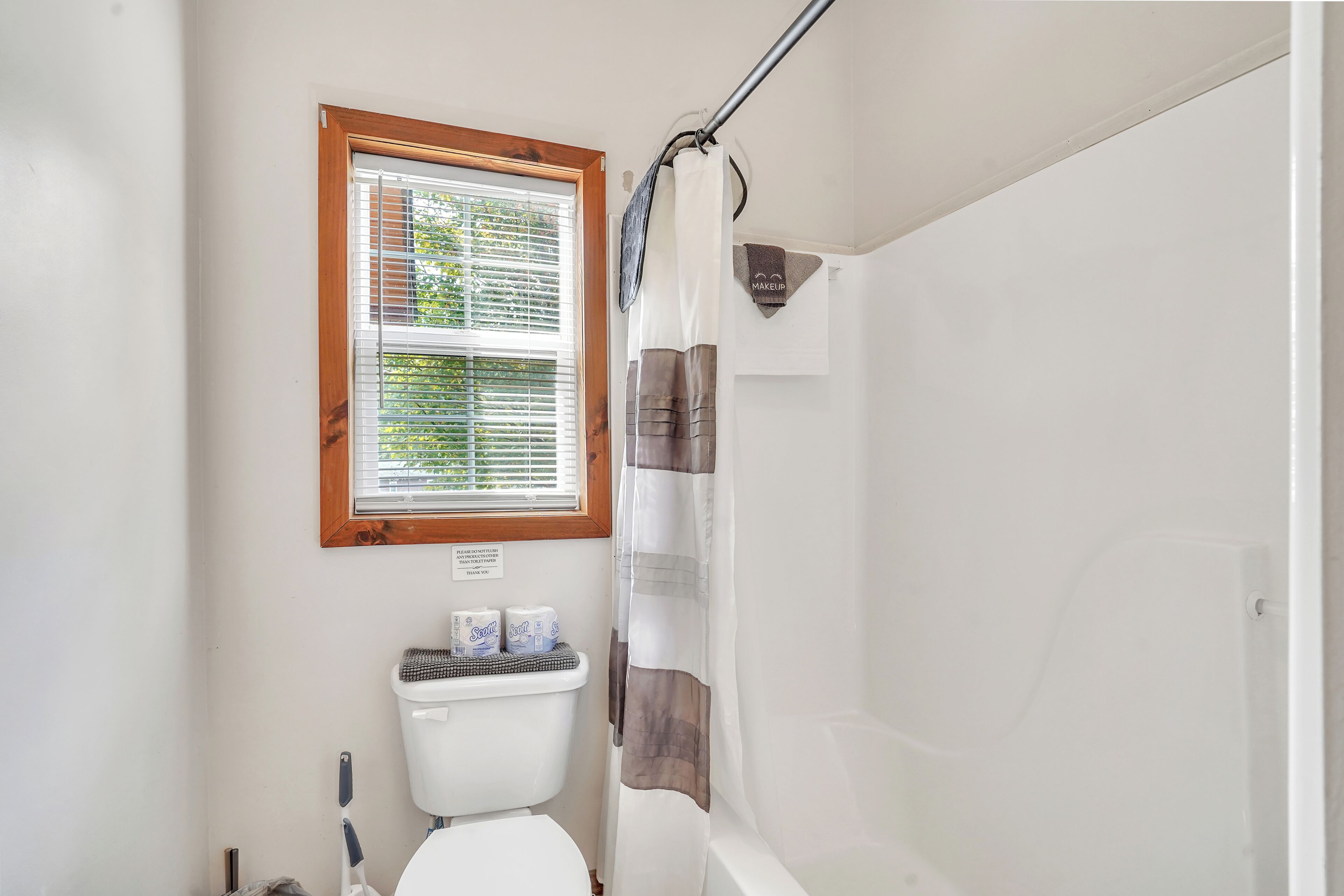 Un baño con inodoro, ventana con persianas, cortina de ducha y un letrero en la pared.