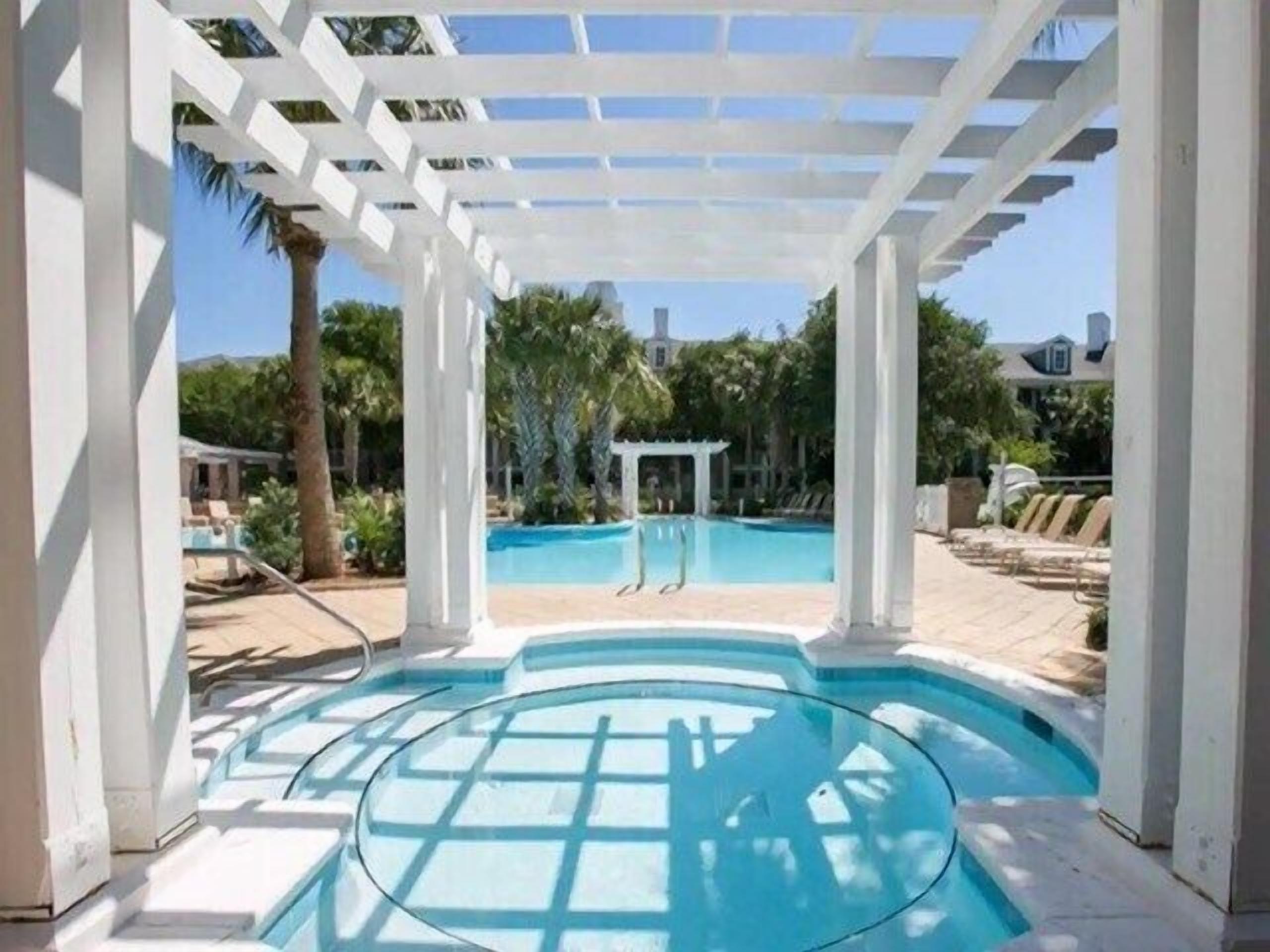 A pool area with a pergola structure, a small pool, and lounge chairs.
