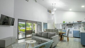 Una sala de estar moderna con un sofá, una mesita y una silla. Hay una zona de cocina con un microondas y una mesa de comedor.