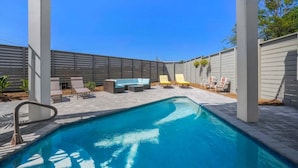 Una piscina con sillones de playa y una tumbona bajo una pérgola.