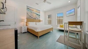 Ein Schlafzimmer mit Bett, Nachttischen, einem Sessel, Deckenventilator und einem Fenster mit Jalousien.