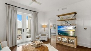 Uma sala de estar com uma televisão grande, um banquinho de vime e um móvel de madeira para televisão.