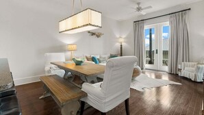 Uma sala de jantar com mesa de madeira, cadeiras brancas e luminária pendente.