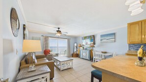 A spacious living area with a balcony, a dining table, and a kitchen area with wooden cabinets. - Summit Treasure 1312–1 Bedroom–Sleeps 5 (Panama City Beach)