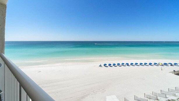 Une vue sur la plage depuis un balcon, avec une rangée de parasols bleus et de chaises longues blanches.
