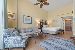 A living room with a sofa, a bed, a coffee table, and a ceiling fan.