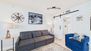 Un salon avec un canapé gris, un fauteuil bleu, un tableau, une ancre décorative et un luminaire au plafond.