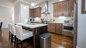 Una cocina moderna con armarios de madera, una campana extractora de acero inoxidable, microondas integrado y una isla grande con taburetes de bar.