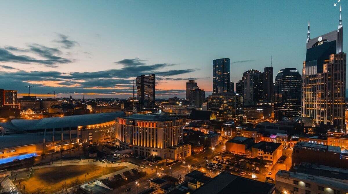 A cityscape at dusk with illuminated buildings and a stadium in the foreground.