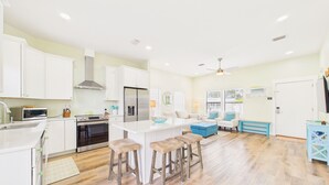 Cocina moderna con armarios blancos, estufa de acero inoxidable y una isla central con taburetes.