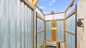Estructura rústica de madera y metal corrugado con zona de ducha, una puerta de madera y un cabezal de ducha metálico.