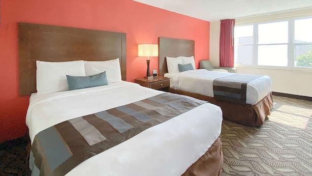 A hotel room with two beds, a red wall, a patterned carpet, and a window with a view. - Super 8 by Wyndham Greensburg/Latrobe (Greensburg)