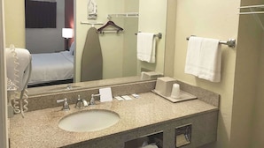 A hotel bathroom with a sink, mirror, towel rack, and a bed visible in the reflection. - Super 8 by Wyndham Greensburg/Latrobe (Greensburg)
