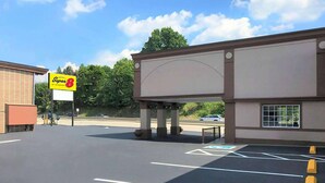 A parking lot with marked spaces, a Super 8 sign, and a building with a large billboard. - Super 8 by Wyndham Greensburg/Latrobe (Greensburg)