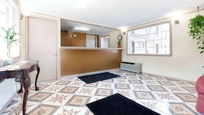 A hotel lobby with patterned flooring, a reception desk, a clock, and a large window. - Super 8 by Wyndham Greensburg/Latrobe (Greensburg)