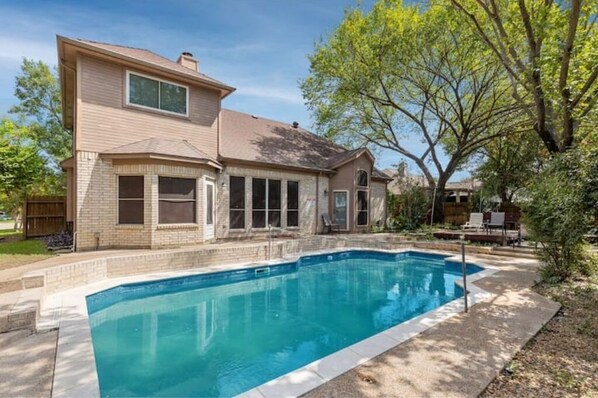 Une maison à deux étages avec une piscine, un patio couvert et un grand arbre dans le jardin.