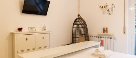 A modern hotel room with a large bed, a flat-screen TV mounted on the wall, a white dresser, and a unique wall decor piece.