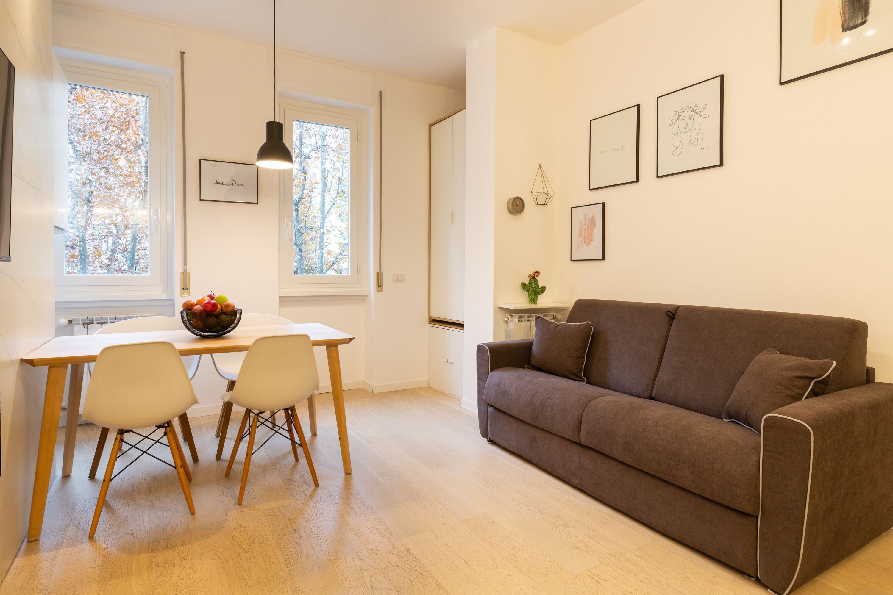 Un salon moderne avec un canapé marron, deux fauteuils blancs, une table à manger en bois et un saladier rempli de fruits.