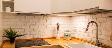 Uma cozinha com armários brancos, backsplash de parede de tijolos, pia, torradeira e um vaso com planta.