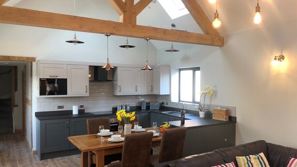 A modern kitchen with wooden beams, pendant lights, and a dining area with a table set for four. - Luxury Secluded Barn With Private Hot Tub (Denbigh)