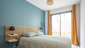 Et soveværelse med seng, sengebord, lampe og et vindue med gardiner.
