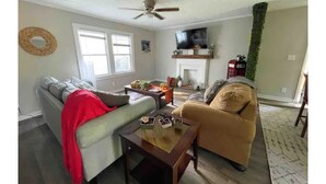 A living room with a grey sofa, a tan armchair, a wooden coffee table, and a television mounted on the wall. - Renovated 2-bedroom home near Columbus Library (Columbus)